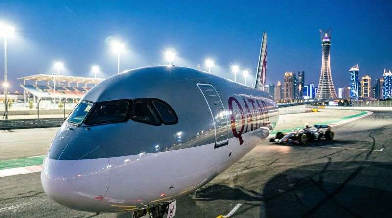 Самолет Qatar Airways на фоне ночного автодрома Лусаил и небоскребов Дохи, акция на билеты Формулы-1 при транзите